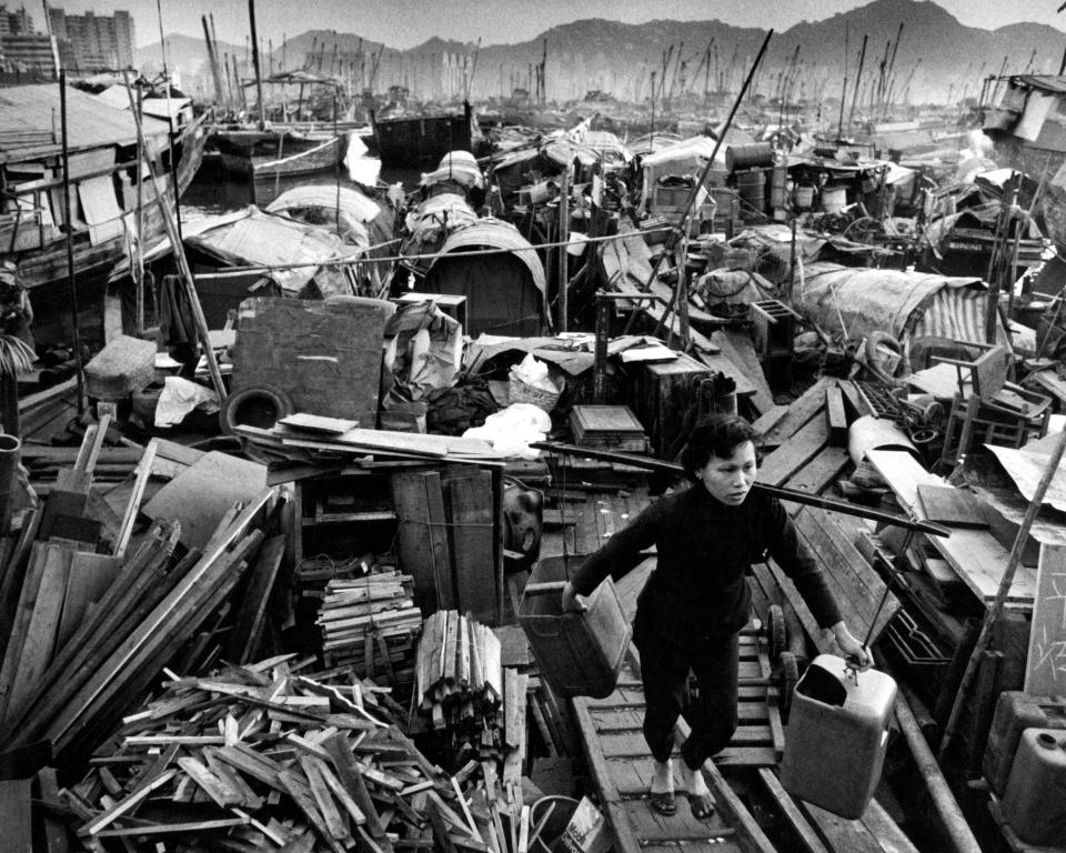 A woman carrying water jugs walks across floating sampans in Hong Kong.