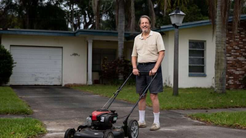Man stands with a lawn mower in front of his home.