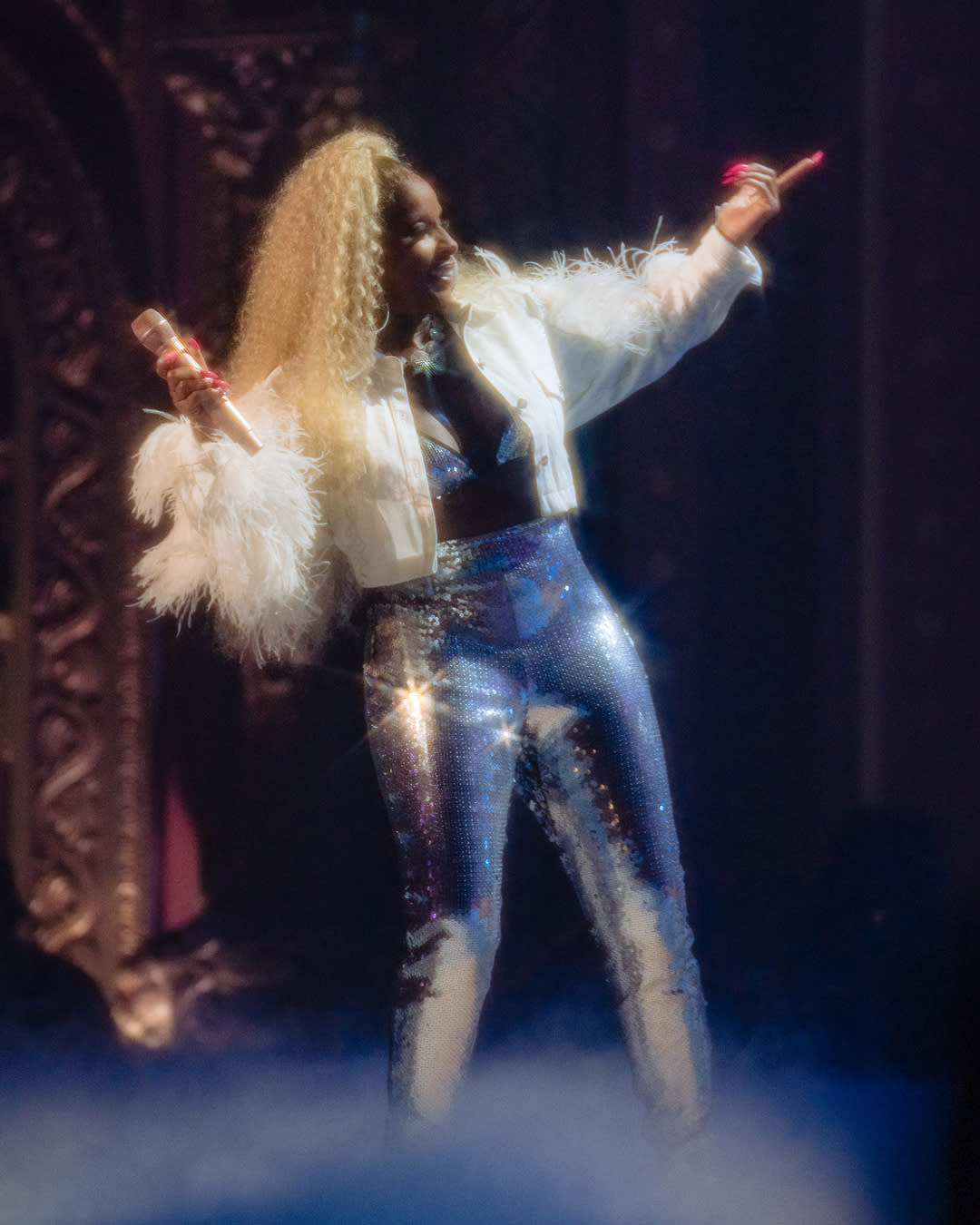 mary j blige smiling on stage in blonde hair, white jacket, and sparkling pants