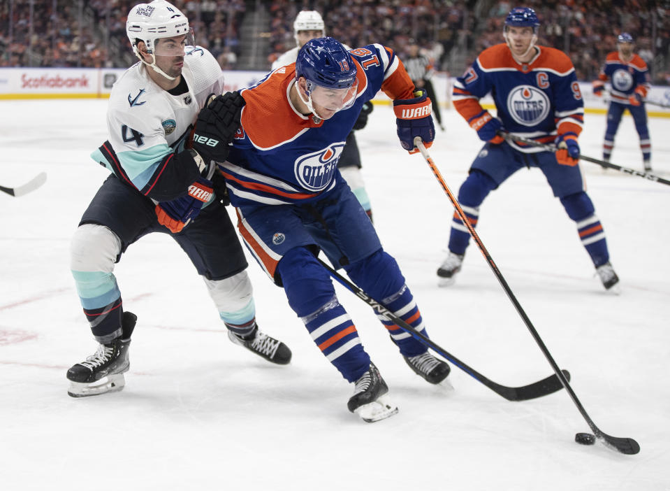 Seattle Kraken's Justin Schultz (4) and Edmonton Oilers' Zach Hyman (18) battle for the puck during the second period of an NHL hockey game, Wednesday, Nov. 15, 2023 in Edmonton, Alberta. (Jason Franson/The Canadian Press via AP)