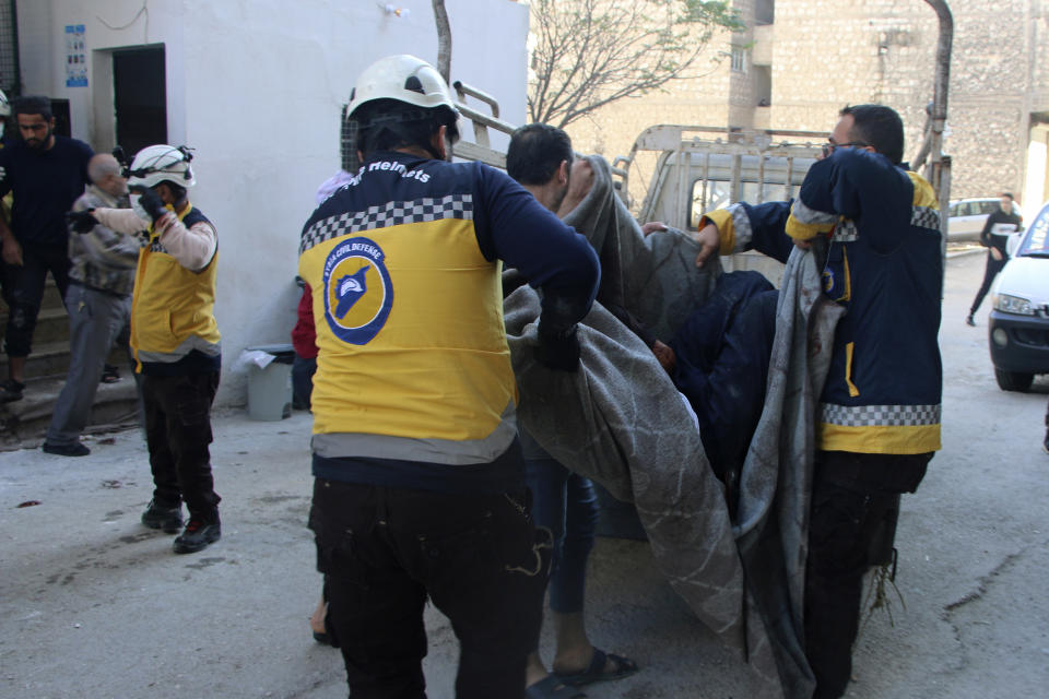 This photo provided by the Syrian Civil Defense White Helmets, which has been authenticated based on its contents and other AP reporting, shows Syrian White Helmet civil defense workers carrying a casualty, in the northern town of Ariha, in Idlib province, Syria, Wednesday, Oct. 20, 2021. Rescue workers reported several people were killed, including children and a woman, in shelling by Syrian government forces on Ariha, in the last rebel enclave in the country's northwest. (Syrian Civil Defense White Helmets via AP)