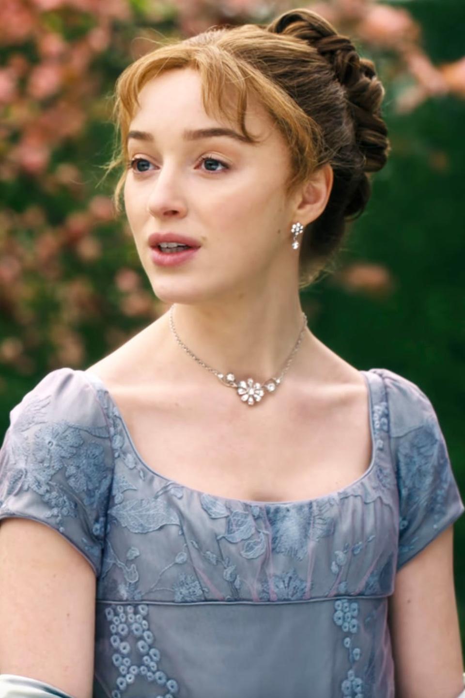 Phoebe Dynevor as Daphne in a Regency-era gown with floral embroidery and jewelry, in a garden setting