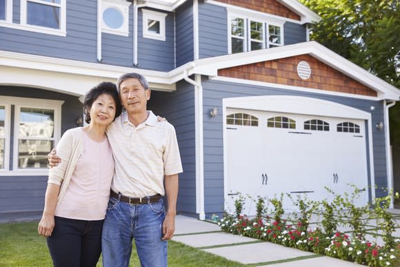 Senior man and woman standing in front of house with arms around each other