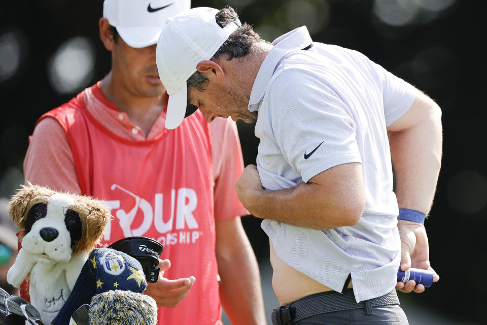 Rory McIlroy, right, applies pain-relieving balm to his back during the first round of the Tour Championship golf tournament at East Lake Golf Club, Thursday, Aug. 24, 2023, in Atlanta. (AP Photo/Alex Slitz)