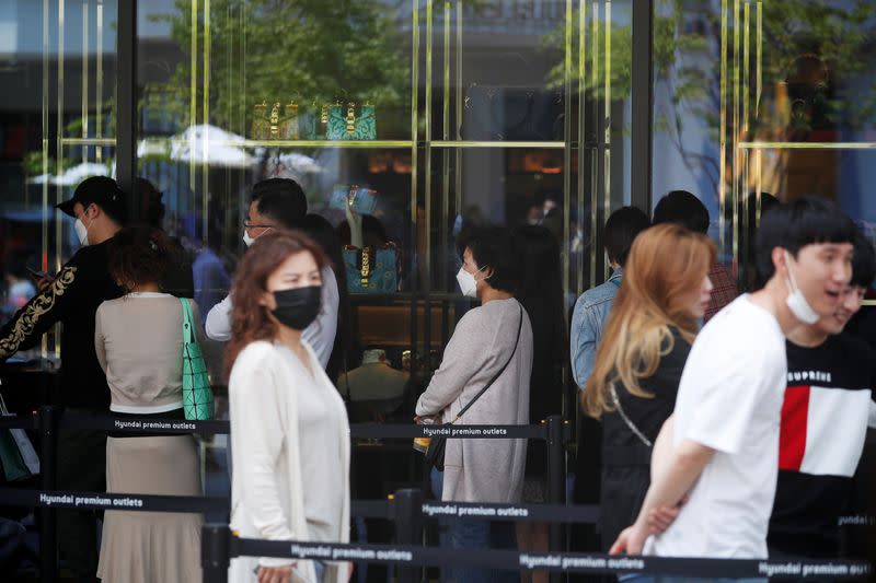 People wearing masks to avoid the spread of the coronavirus disease (COVID-19) wait in a line to get into a luxury shop at an outlet mall in Gimpo