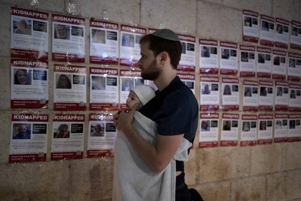 A man holds his baby as he looks at posters of the men, women and children held hostage by Hamas in the Gaza Strip, during a vigil marking 30 days since the Oct. 7 Hamas attack that started the fighting, in Jerusalem, Israel Sunday, Nov. 5, 2023. (AP Photo/Maya Alleruzzo)