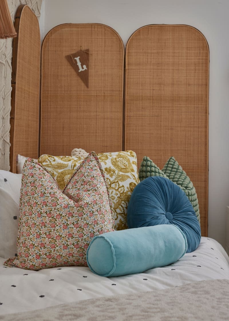 Natural folding screen behind twin bed with throw pillows in white bedroom.