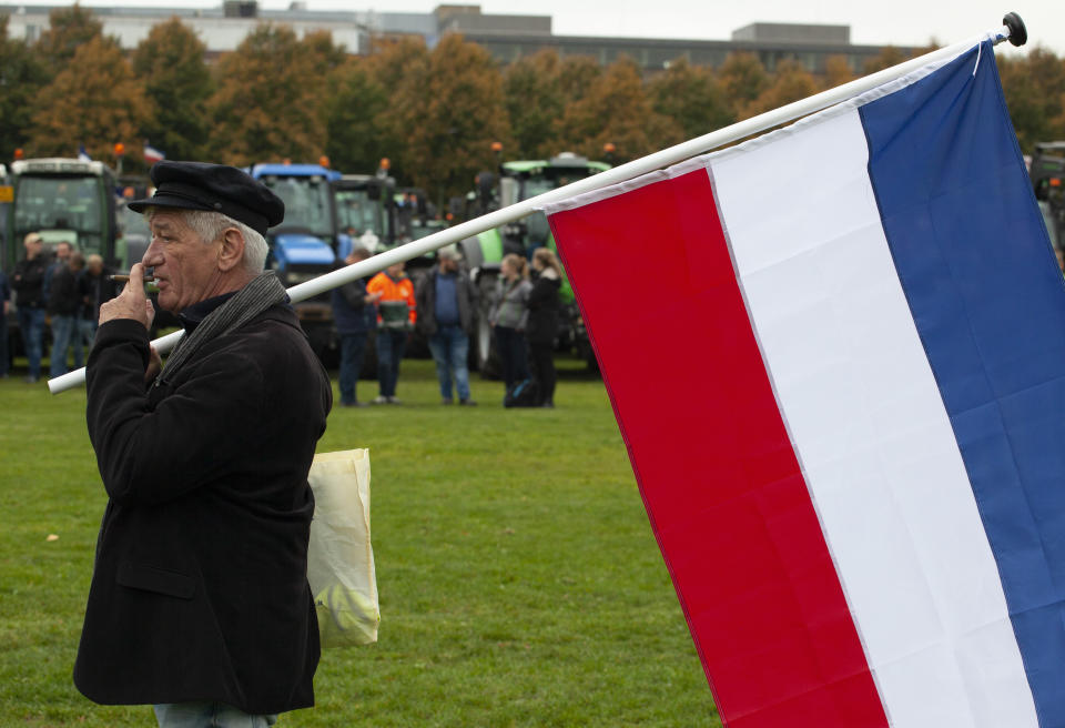 A protestor smokes a cigar when carrying the Dutch flag in The Hague, Netherlands, Wednesday, Oct. 16, 2019. Thousands of Dutch farmers protest over the Netherlands efforts to drastically reduce emissions of greenhouse gases. Among the farmers' demands are that the government does not further reduce the number of animals they can keep. (AP Photo/Peter Dejong)