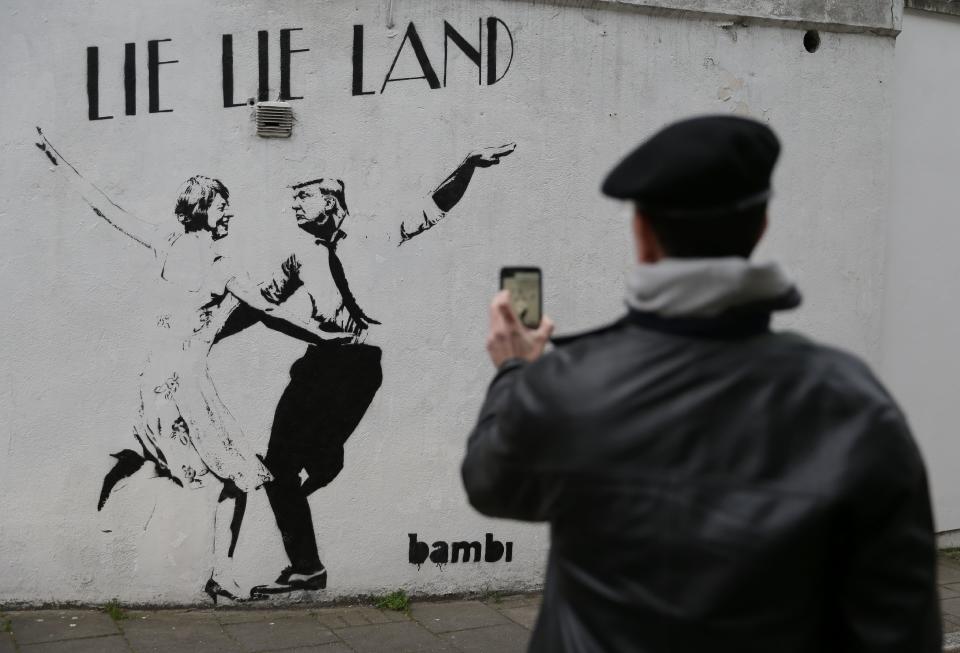 A man takes a picture of a mural by English street artist Bambi depicting British Prime Minister Theresa May dancing with US President Donald Trump in London on February 22, 2017.