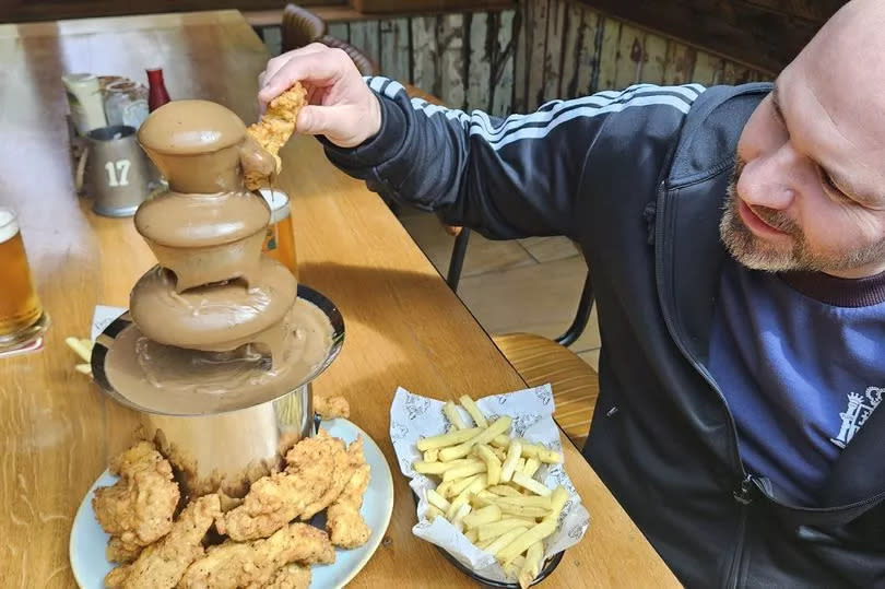 PIC FROM KENNEDY NEWS AND MEDIA (PICTURED: EXECUTIVE CHEF AND COMPANY DIRECTOR GARY EVANS, 40, DIPPING A PIECE OF CHICKEN INTO THE GRAVY FOUNTAIN) A pub is sending fried chicken fans into meltdown by launching a giant GRAVY FOUNTAIN with a monster portion of 30 chicken tenders to dip into it. The Leopard in Nantwich, Cheshire, has gone viral after revealing they're set to serve a litre of home-made gravy in a 15-inch tall fountain for hungry punters to dip fried chicken and fries into. Videos of the Fried Chicken Fountain show curtains of the condiment flowing from the heated spring, while a diner smothers the boozer's 'Leopard Fried Chicken' in it. DISCLAIMER: While Kennedy News and Media uses its best endeavours to establish the copyright and authenticity of all pictures supplied, it accepts no liability for any damage, loss or legal action caused by the use of images supplied and the publication of images is solely at your discretion. SEE KENNEDY NEWS COPY - 0161 697 4266 -Credit:Kennedy News and Media