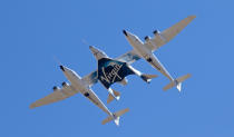 FILE - In this Thursday, Feb. 13, 2020 file photo, Virgin Galactic's VSS Unity departs Mojave Air & Space Port in Mojave, Calif. for the final time as Virgin Galactic shifts its SpaceFlight operations to New Mexico. Virgin Galactic's spaceship VSS Unity, tucked under the wing of its special carrier aircraft, headed east from Southern California on a long-awaited ferry flight to its new home in New Mexico where it will be prepared for commercial operations carrying tourists on hops into space, the company said. (Matt Hartman via AP)