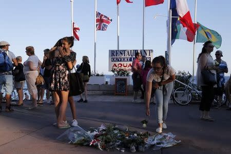 People react near flowers placed on the walkway in tribute to victims, two days after an attack by the driver of a heavy truck who ran into a crowd on Bastille Day killing scores and injuring as many on the Promenade des Anglais, in Nice, France, July 16, 2016. REUTERS/Pascal Rossignol