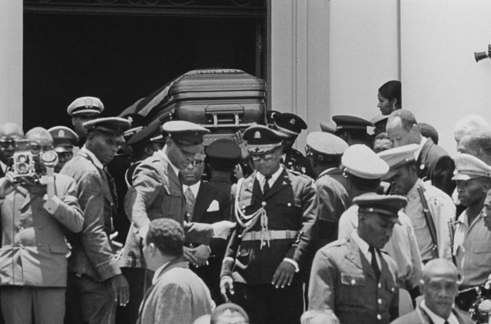 Government officials carry a casket.