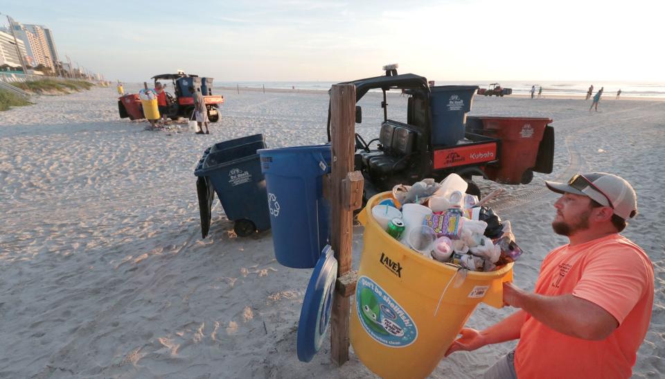 A CFB Outdoors employee empties trash cans in front of the boardwalk, Tuesday morning, July 5, 2022, as crews and volunteers pick up the discarded fireworks and other trash left after the July Fourth celebration.