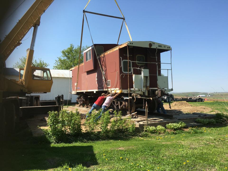 Jim Dotzenrod and a friend help place the train caboose on a set of tracks near his Iowa home.