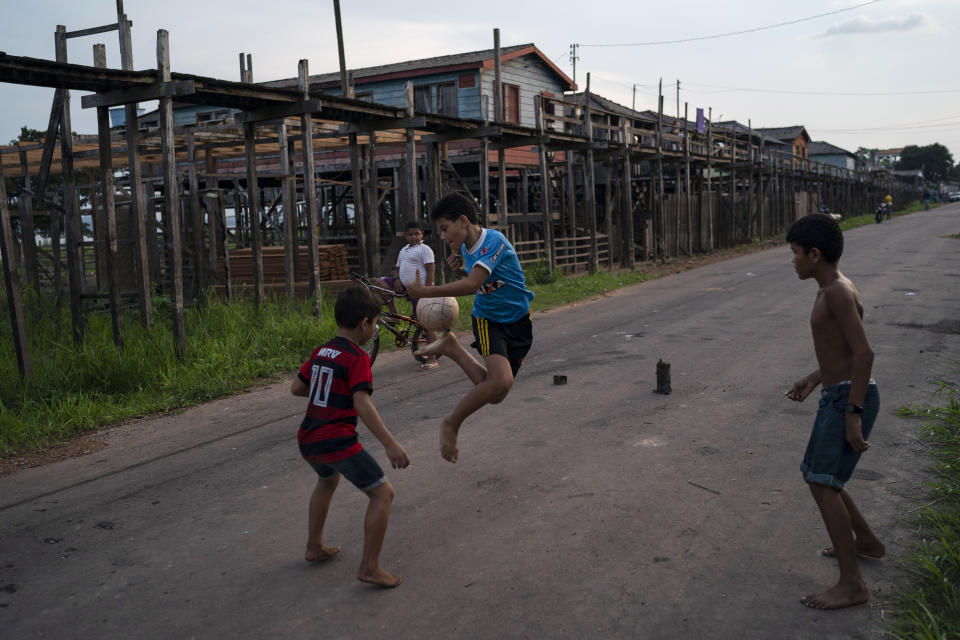 In this Nov. 27, 2019 photo, boys play soccer next to stilt houses at the Vila Nova neighborhood in Itaituba, Para state, Brazil. Carved through jungle during Brazil's military dictatorship in the 1970s, the Trans-Amazon highway that runs through town was built to bend nature to man's will in the vast hinterland. (AP Photo/Leo Correa)