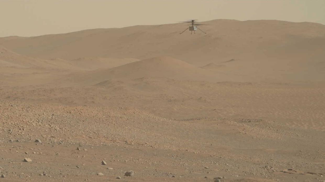  a small robotic helicopter hovers in front of a reddish-brown mountain on mars 