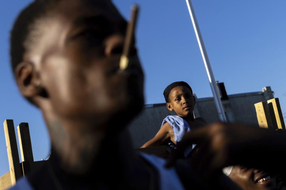 People look on as police officers question a boy during a vigil for Antonio Lee, Friday, Aug. 18, 2023, in Baltimore. Lee, 19, was shot and killed while squeegeeing in Baltimore. (AP Photo/Julia Nikhinson)