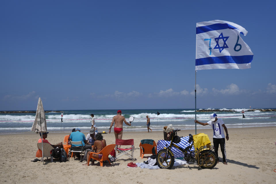 A man places an Israeli flag on the beach during Israel's Independence Day celebrations in Tel Aviv, Tuesday, May 14, 2024. Israelis are marking 76 years since Israel's creation. (AP Photo/Ohad Zwigenberg).