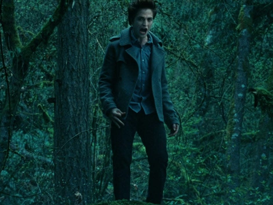 Edward wearing a gray jacket and standing in the forest in twilight