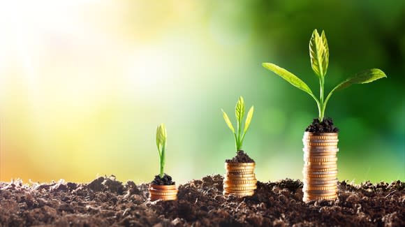 Successively larger stacks of coins in dirt with plants growing out of the tops, dividend growth concept