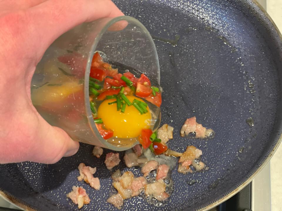 hand carefully pouring eggs into a frying pan with bacon