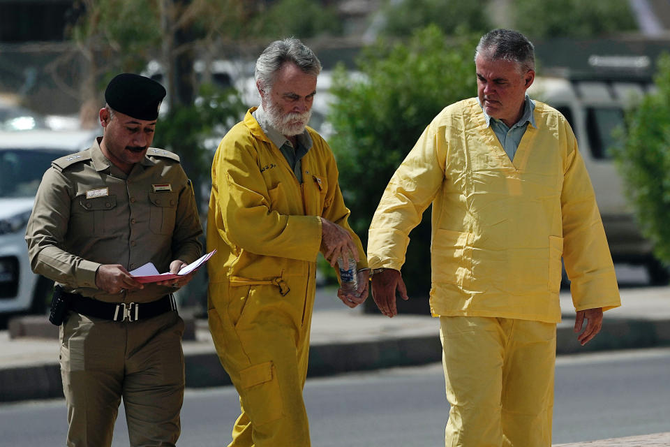 Volker Waldmann, right, and Jim Fitton, center, are handcuffed as they walk to a courtroom in Baghdad, Iraq, Sunday, May 22, 2022. Waldmann and Fitton, accused of smuggling ancient shards out of Iraq, appeared in a Baghdad court Sunday, telling judges they had not acted with criminal intent and had no idea they might have broken local laws. (AP Photo/Hadi Mizban)