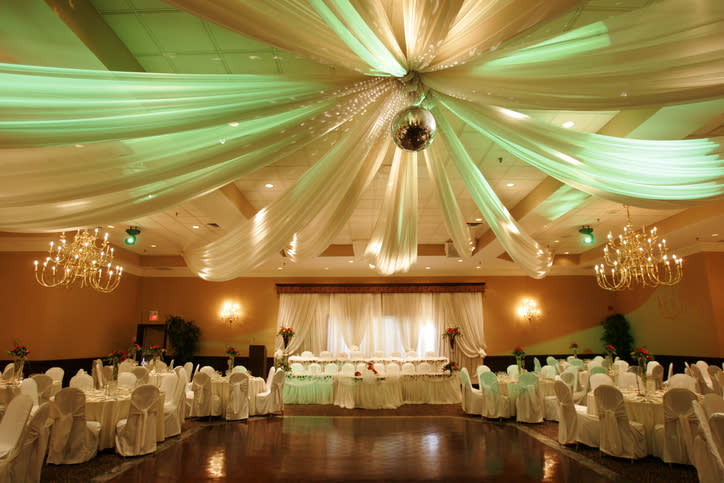 Elegantly decorated banquet hall with draped fabric, chandeliers, and tables adorned with white linens set for a formal event