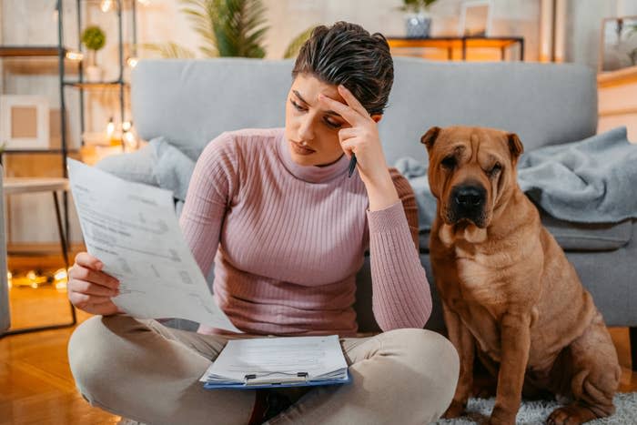 Worried young woman checking her finances while sitting on the floor at home, with her cute shar-pei dog