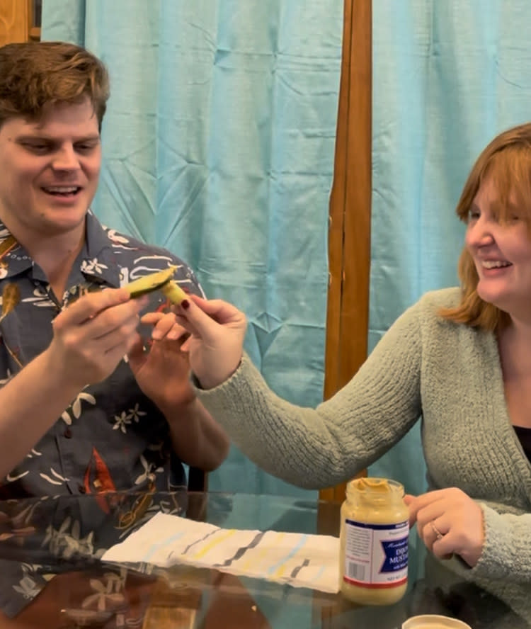 the couple holding up pickles dipped in mustard