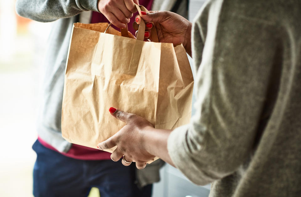 Woman holding paper bag with take out food, home delivery, food order, takeaway. source: Getty