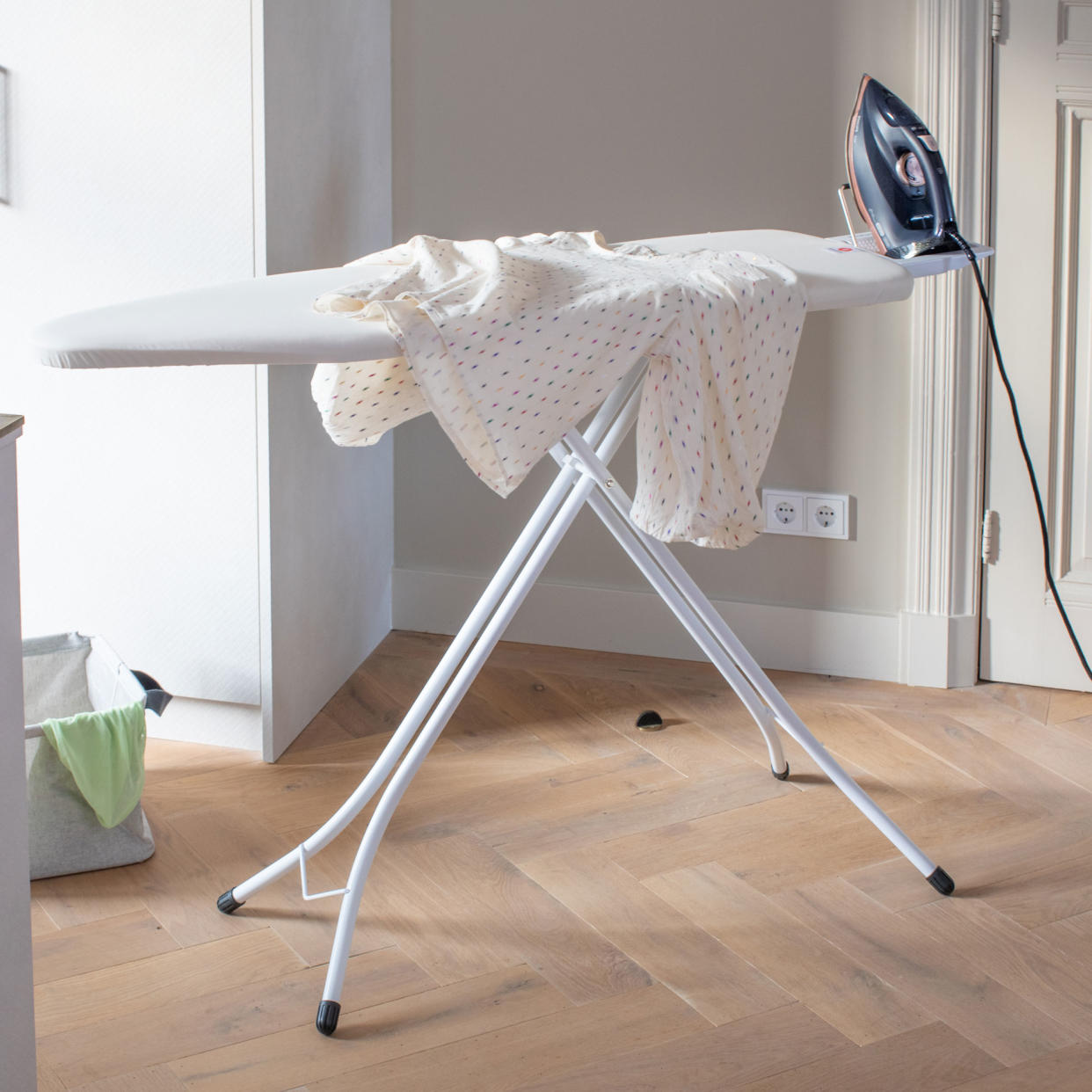  Ironing board with a sheet and iron in a kitchen with herringbone wood floor. 