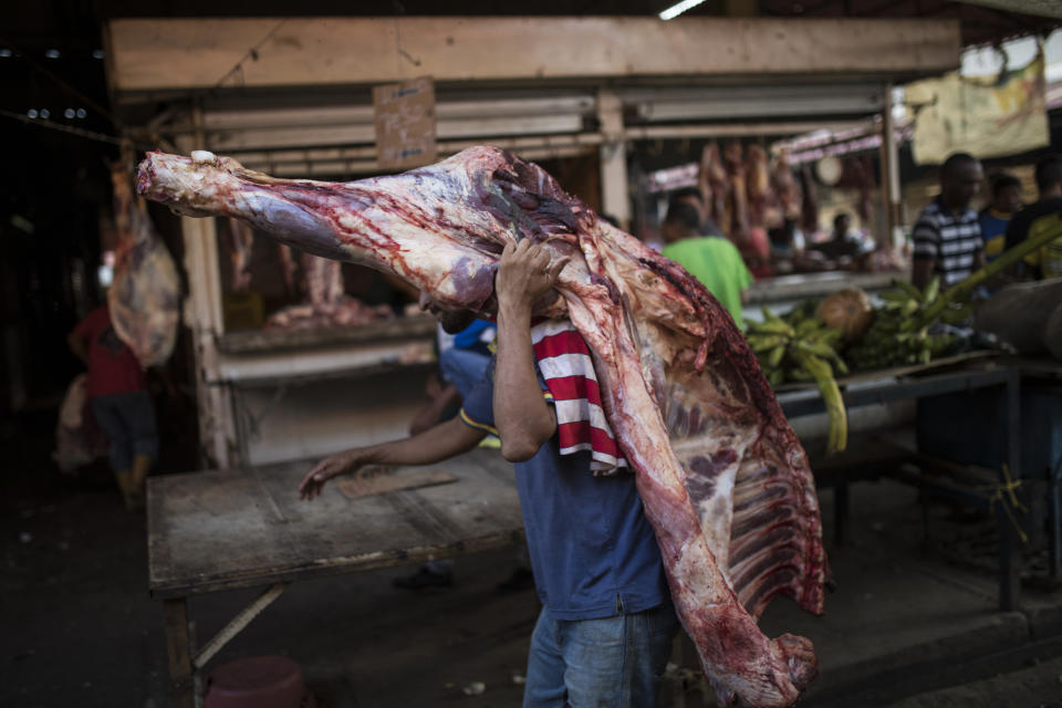 A vendor carries beef to a butcher shop at the flea market in Maracaibo, Venezuela, May 16, 2019. He'll have to sell it quickly, since perishables go bad quickly without refrigeration in Maracaibo's suffocating temperatures. (AP Photo/Rodrigo Abd)