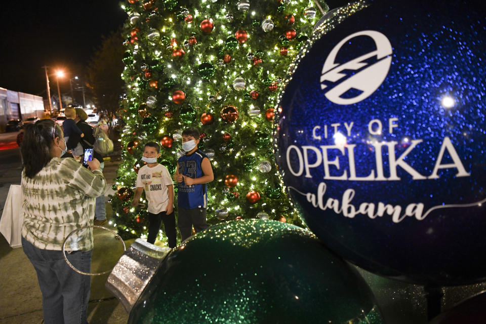 Denise Culpepper, from left, takes a photo of Christopher and Caleb King near the Christmas tree Friday, Dec. 11, 2020, during Christmas in a Railroad Town festivities in downtown Opelika, Ala. Doctors and nurses caring for the sickest COVID-19 patients are doing what they can to get through the holidays while neighbors and friends indulge in Christmas parades and tree lightings. (AP Photo/Julie Bennett)