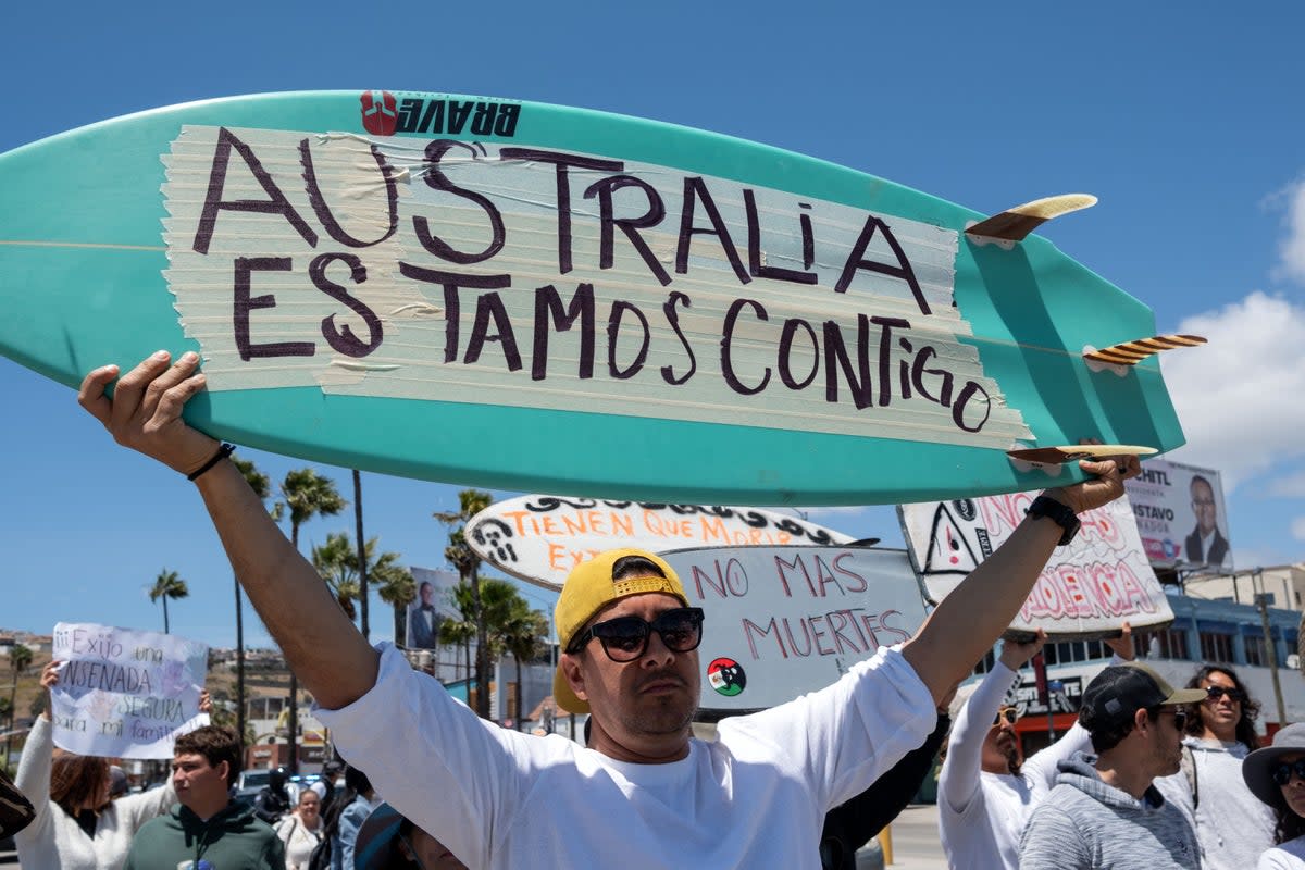 A man raises a surfboard reading ‘Australia We Are With You’ next to members of the surfing community protesting against insecurity after two Australians and an American surfer went missing during a surfing trip, in Ensenada, Baja California state, Mexico, in May (Guillermo Arias / AFP via Getty Images)
