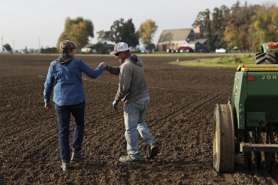 Gayle Goschie fist bumps Eloy Luevanos after setting up a harrow to be pulled behind a tractor and grain hopper in preparation for planting winter barley at Goschie Farms in Mount Angel, Ore., Tuesday, Oct. 31, 2023. Fall is the off-season, but recently, her farming team has been adding winter barley, a relatively newer crop in the world of beer, to their rotation. In the face of climate change, Goschie will need all the new strategies the farm can get to sustain what they produce and provide to local and larger breweries alike. (AP Photo/Amanda Loman)