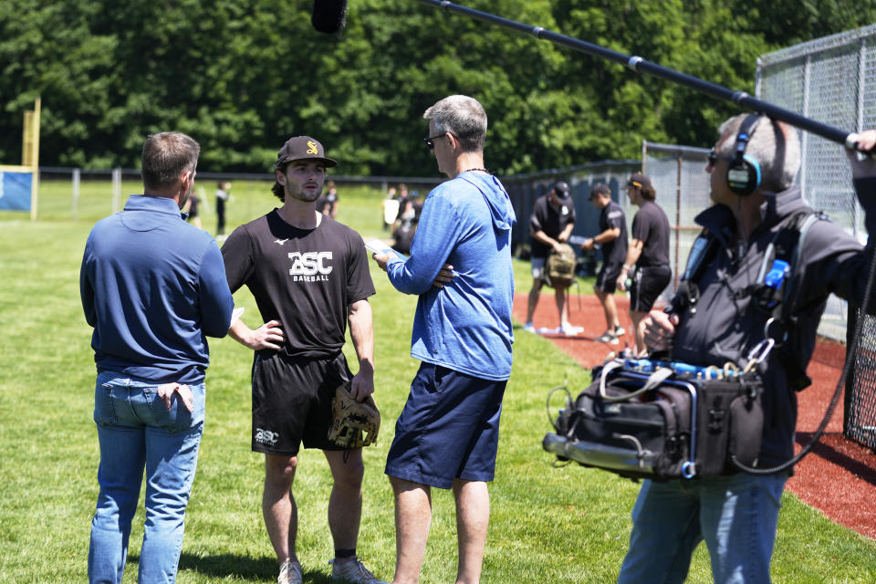 Birmingham-Southern infielder Andrew Dutton, center, talks with reporters as a member of a documentary team collects audio, right, Thursday, May 30, 2024, in Kirtland, Ohio. On Friday, the Panthers will continue an unexpected, uplifting season that has captured hearts across the country by playing in the Division III World Series on the same day the liberal arts college founded on the eve of the Civil War shuts its doors. (AP Photo/Sue Ogrocki)