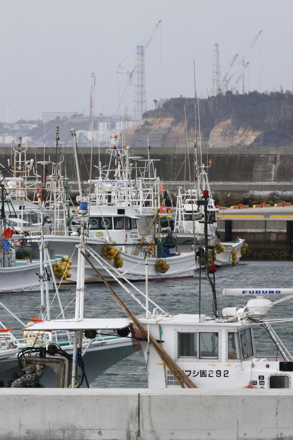 Fishing boats are seen at Ukedo port with a backdrop of Fukushima Daiichi nuclear power plant in Namie town, Fukushima prefecture, northeastern Japan, Tuesday, April 13, 2021, Japan's government decided Tuesday to start releasing massive amounts of treated radioactive water from the wrecked Fukushima nuclear plant into the Pacific Ocean in two years - an option fiercely opposed by local fishermen and residents. (Yusuke Ogata/Kyodo News via AP)