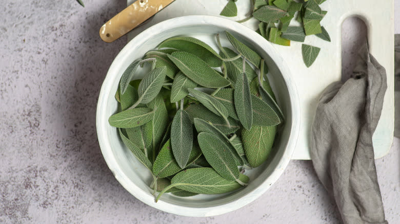 Sage leaves in a bowl next to knife and cut leaves