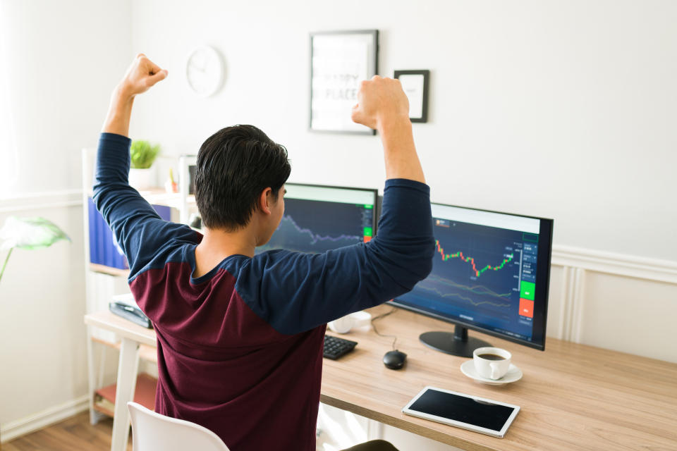 Happy man seen from behind celebrating the stock market rise. Cheerful young man investing in cryptocurrency at home