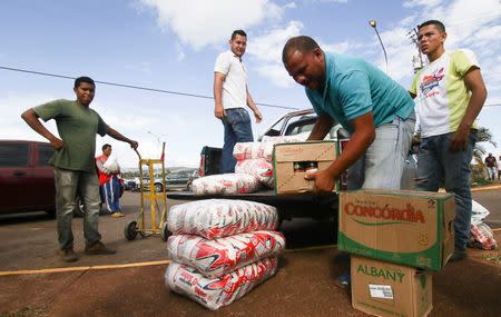 Men load boxes of food onto the back of a pick-up truck, after arriving from Brazil, in front of the bus terminal in Santa Elena de Uairen, Venezuela August 2, 2016. REUTERS/William Urdaneta