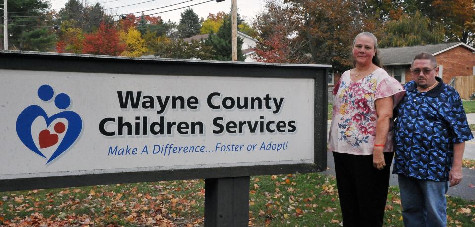 Kimberly and Lonnie Blevins stand by the foster program sign in front of the Kinney Building on Burbank Road in Wooster. They have been in the foster family program for 20 years.