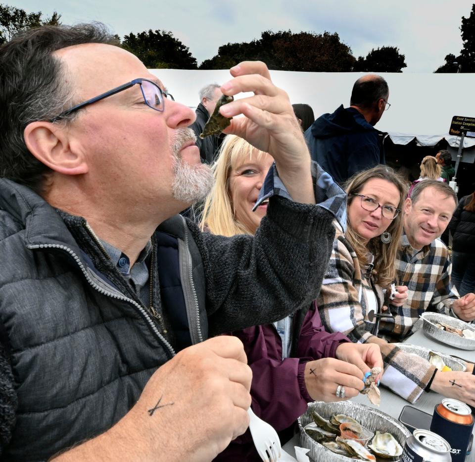 Tim Pellegrin of Brewster downs an oyster in October 2023 during Wellfleet's OysterFest, to the delight of Jenn Peto of Brewster and friends Cindy Richards and Jason MacFarland of Ocean City, New Jersey. OysterFest isn't until the fall, but a new "Shuck and Shop" May 26 showcases the town's famous shellfish.