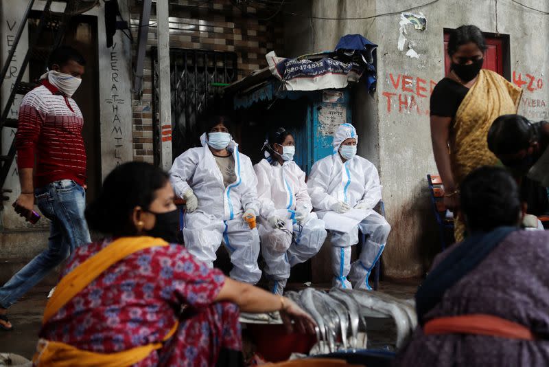 Health workers in personal protective equipment rest during a check up campaign for the coronavirus disease (COVID-19) at a slum area in Mumbai