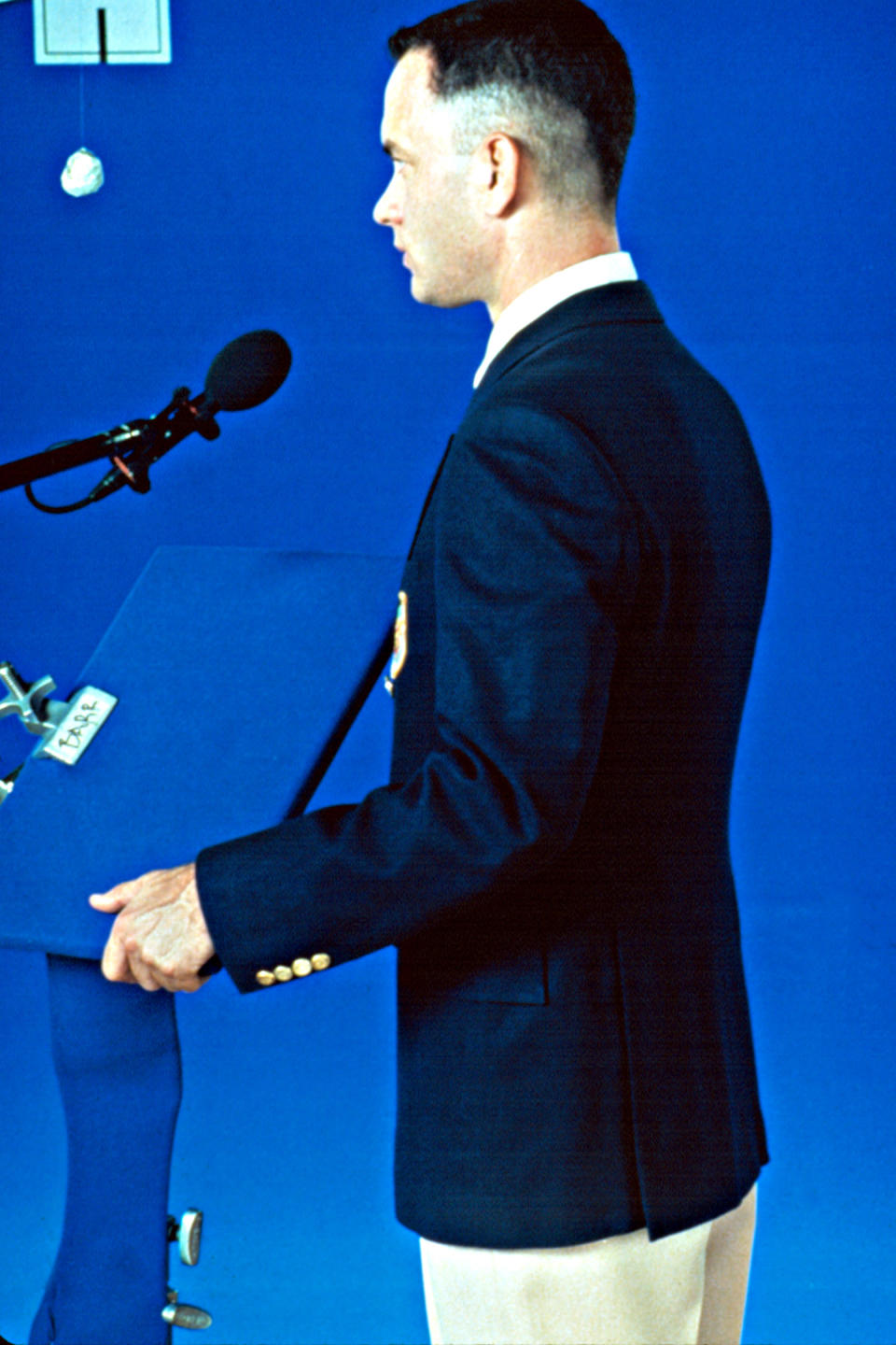 Tom Hanks in a suit speaks at a podium during a press event or speech