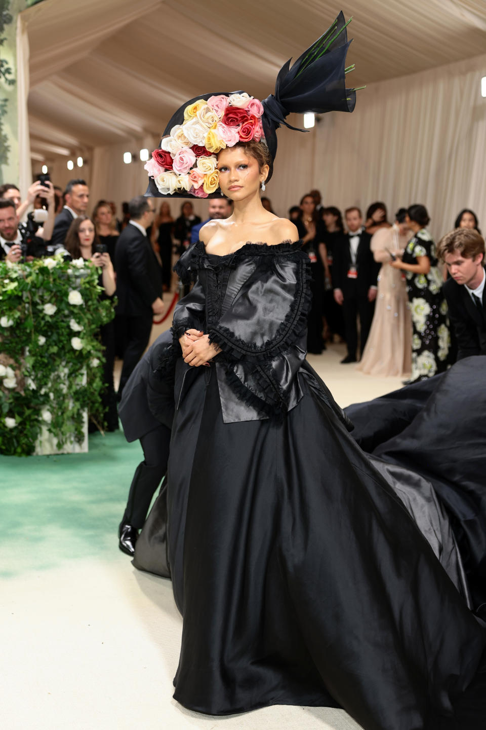 Zendaya in a black gown with a pink floral headpiece at an event