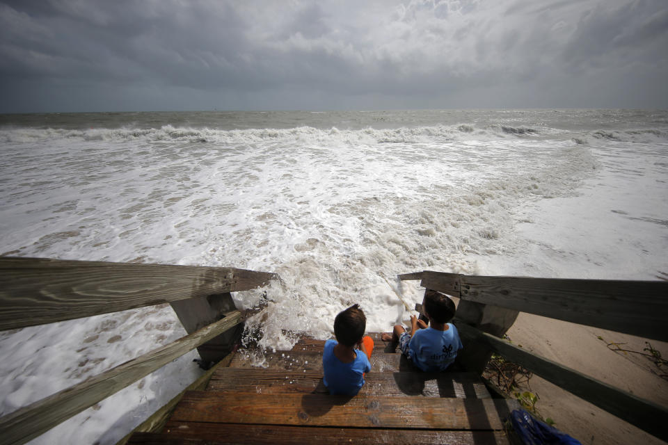 Maximus Modert, left, and Tyde Modert, of Fort Pierce, Fla., sit on boardwalk steps at the edge of a high surf from the Atlantic Ocean, in advance of the potential arrival of Hurricane Dorian, in Vero Beach, Fla., Monday, Sept. 2, 2019. (AP Photo/Gerald Herbert)
