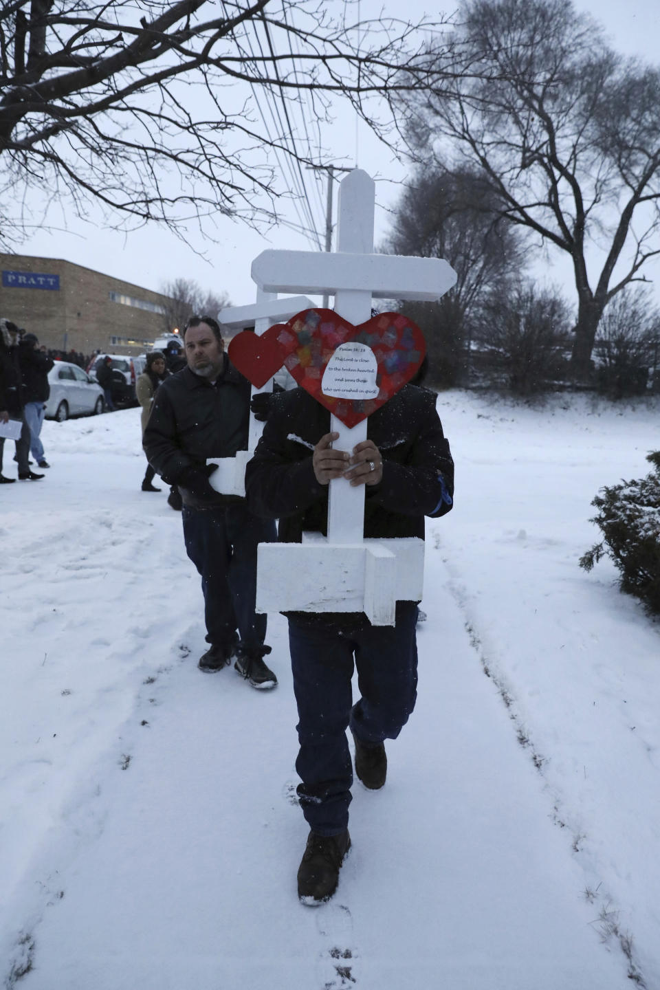 Casildo Cuevas holds a victim's cross as he walks to the Aurora police station after a makeshift memorial Sunday, Feb. 17, 2019, in Aurora, Ill., near Henry Pratt Co. manufacturing company where several were killed on Friday. Authorities say an initial background check five years ago failed to flag an out-of-state felony conviction that would have prevented a man from buying the gun he used in the mass shooting in Aurora. (AP Photo/Nam Y. Huh)