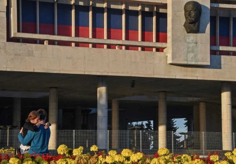 A couple embraces in front of fences at Lenin Memorial Museum that protect visitors after several massive panels dropped off the facade