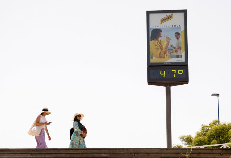 Dos personas pasan junto a un termómetro que marca 47 grados en una calle de Sevilla, España.